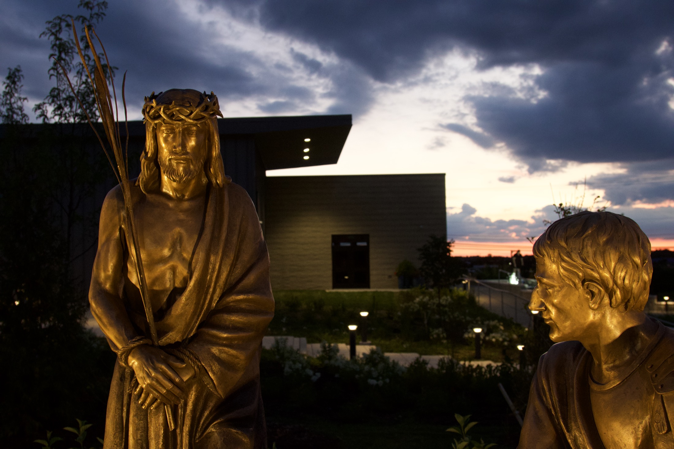 A close profile of a bronze figure of Christ's face, caught in golden-hour light.
