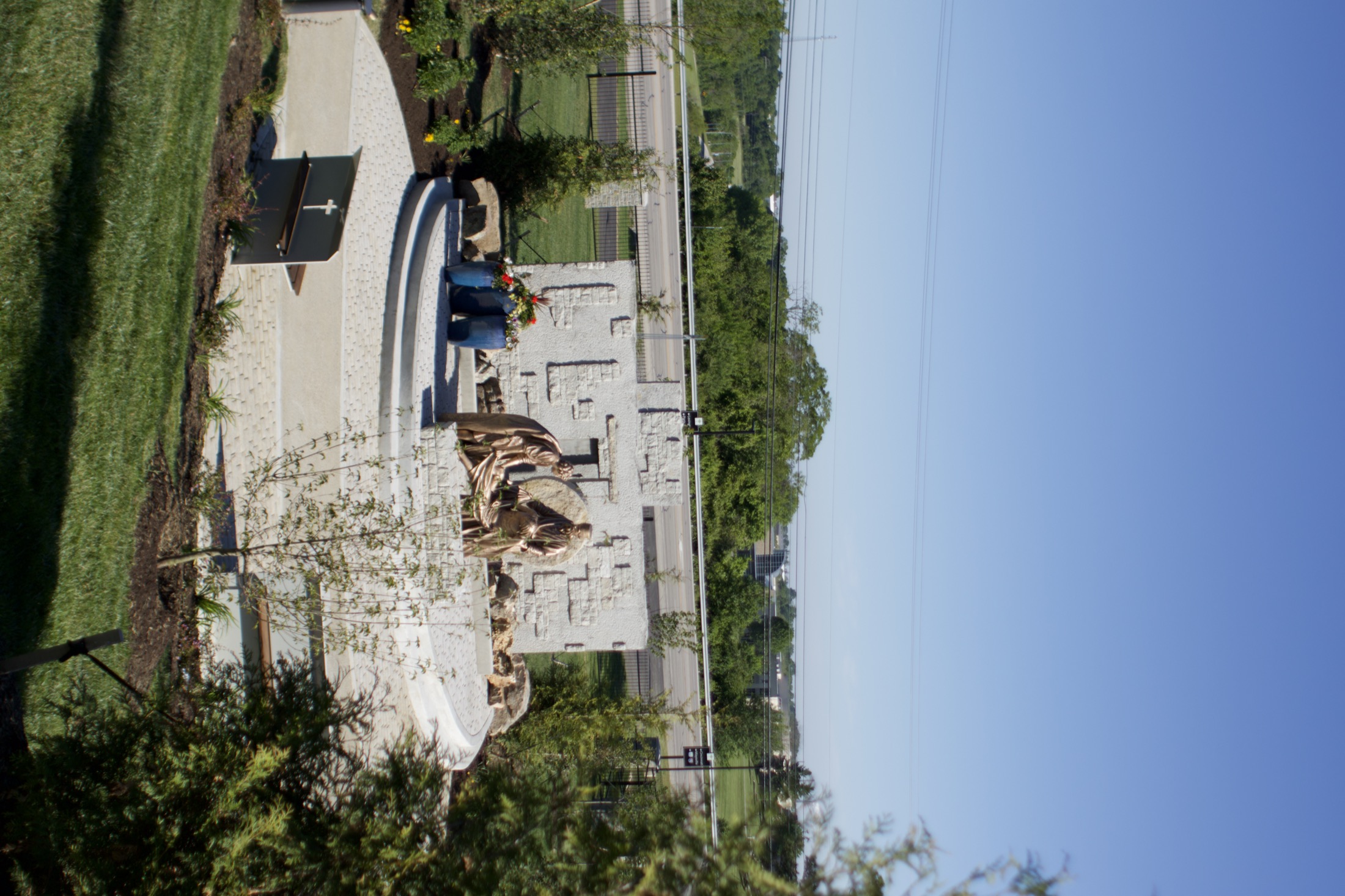 A wide view of the grounds, showing a curved stone gathering area, benches, and the surrounding countryside.