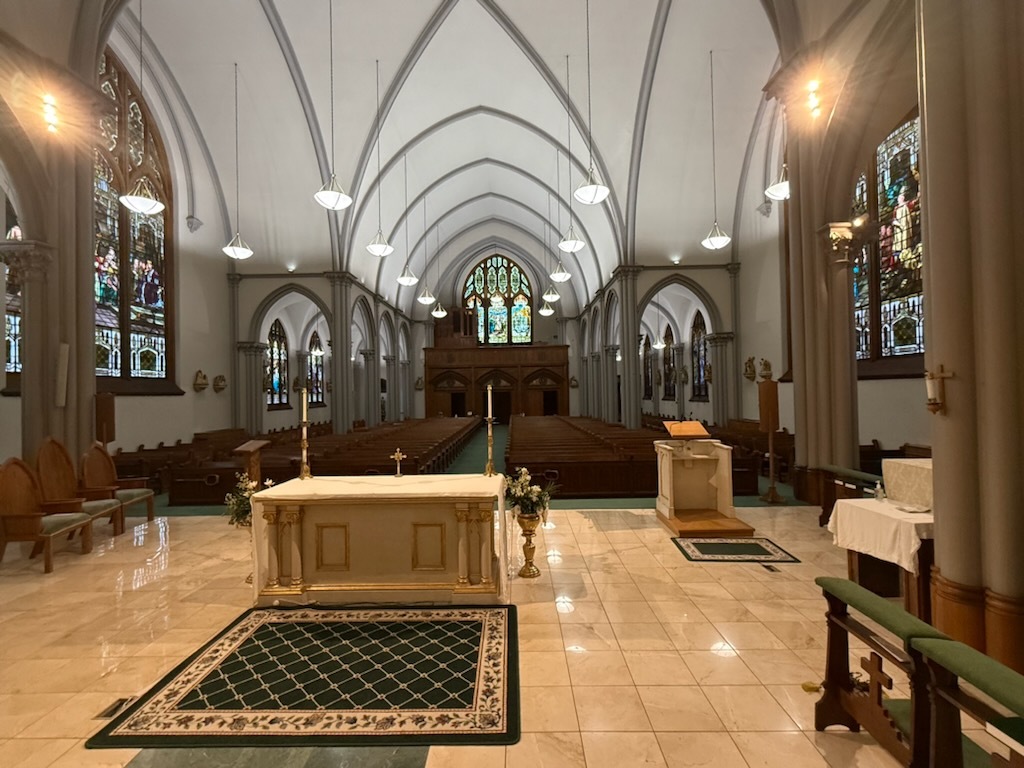 St. Patrick’s ornate white-and-gold high altar and statuary beneath the sanctuary’s stained-glass windows, with the marble altar table and its carved Last Supper relief in the foreground.