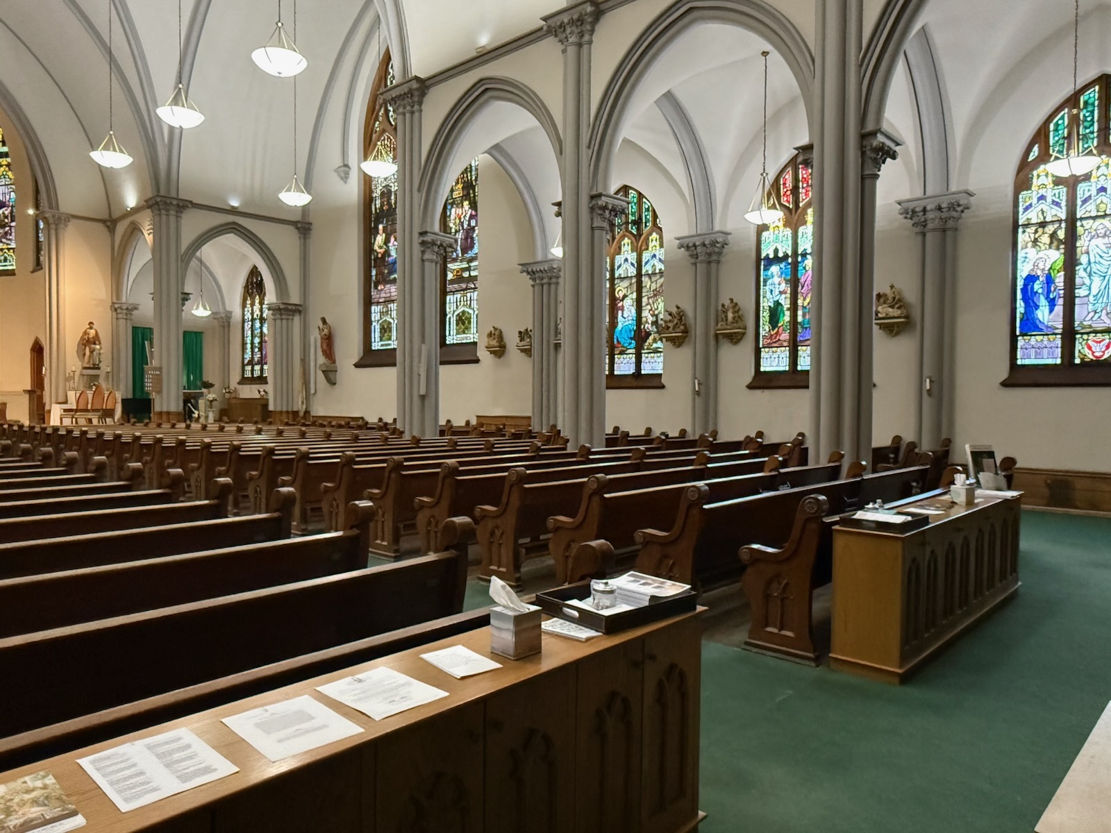 The rear choir loft and organ pipes beneath a towering Gothic stained-glass window, above the church’s three arched entrance portals.