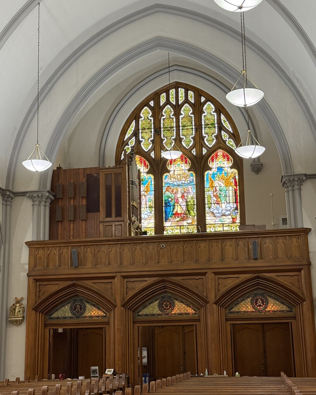A side aisle lined with pointed-arch stained-glass windows and slender grey columns, above rows of wooden pews.